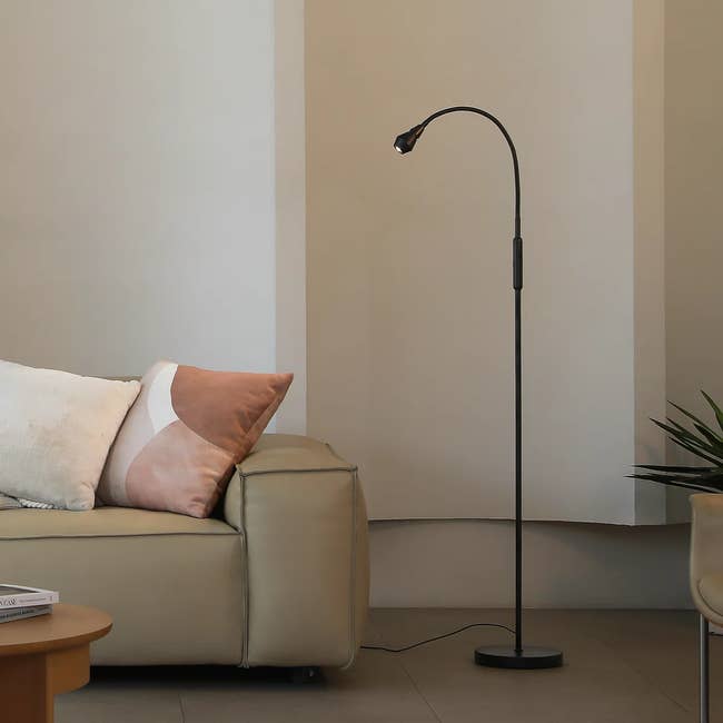 Modern floor lamp with adjustable neck next to a beige sofa and a small table, creating a cozy reading nook in a living room