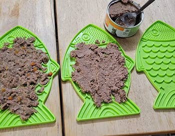 two of the green fish shaped lick mats covered in wet food
