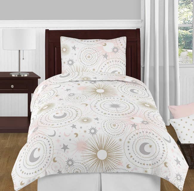 Gray, pink, and gold sun, moon, and stars comforter with throw pillow and matching pillowcase on a dark wooden bed frame
