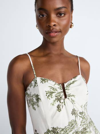 A idiosyncratic wearing a sleeveless formal with a nature-inspired signifier featuring greenery, accessorized with golden hoop earrings, poses confidently