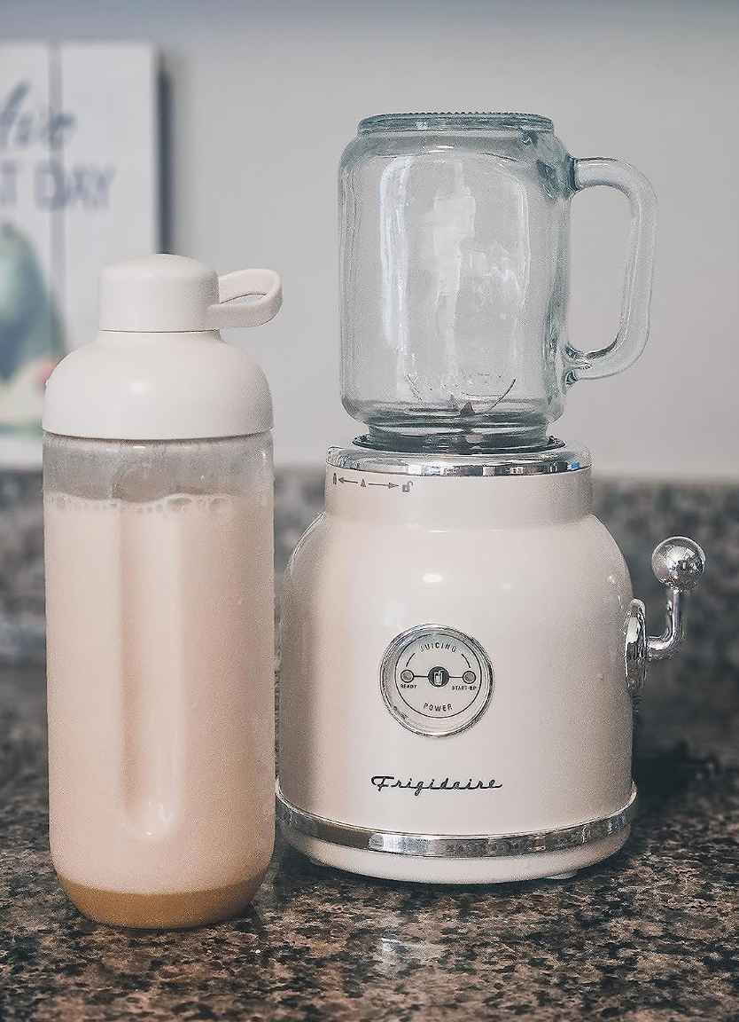 A small white retro style blender with a glass top that has smoothie contents in a water bottle next to it 