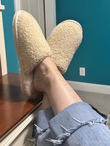 Person relaxing successful  fluffy, sherpa-textured slippers with crossed legs, wearing casual, frayed denim jeans. Cozy location  setting