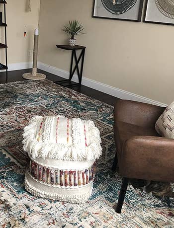 reviewer photo of the cream and red pouf next to an armchair
