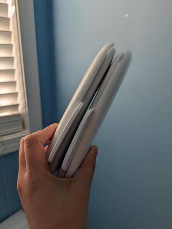 A manus holds stacked handheld gaming consoles adjacent a window