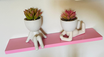 Reviewer image of two white body-shaped vases with fake succulents inside on top of a pink floating shelf