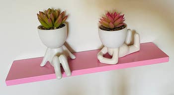 Reviewer image of two white body-shaped vases with fake succulents inside on top of a pink floating shelf