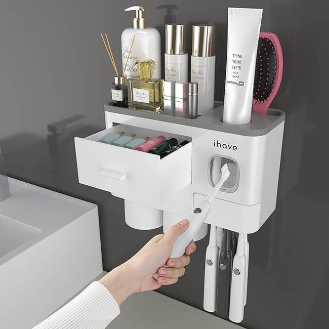 A wall-mounted organizer with compartments holding personal care items and a hand pulling out a drawer