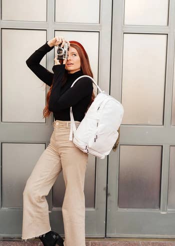 model wearing the white backpack while using a camera