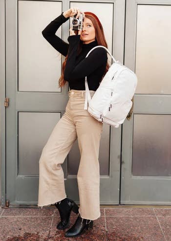 model wearing the white backpack while using a camera