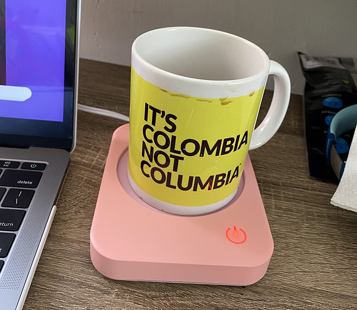 a reviewer photo of a mug sitting on a pastel pink mug warmer 