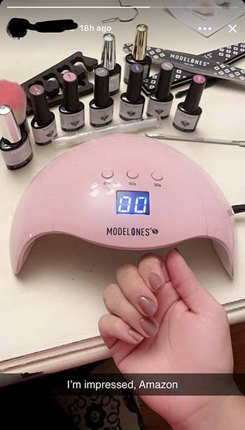 reviewer photo of their painted nails next to a pink UV lamp and a bunch of polish bottles and nail tools with the caption 