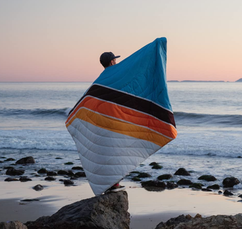 back of model holding the colorful striped blanket near the ocean
