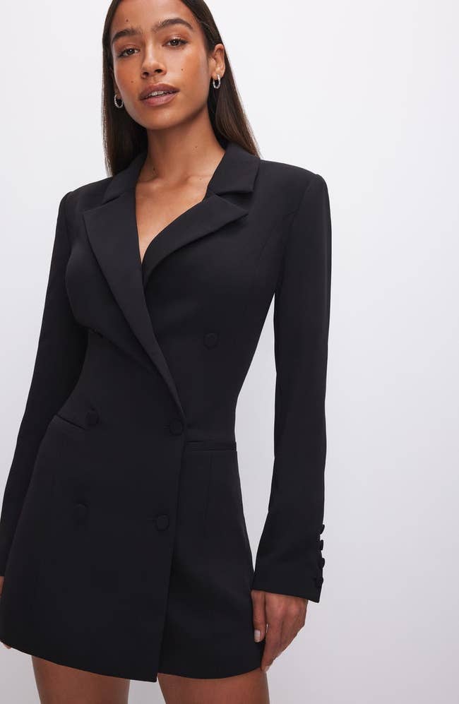 Model wearing a black blazer dress with button details, suitable for office or formal wear