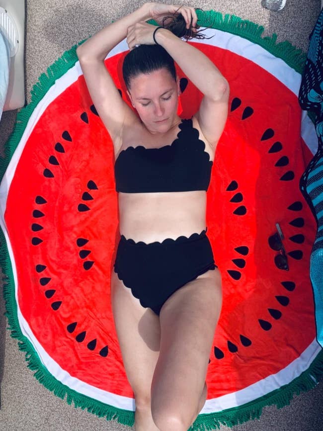 reviewer wearing the black bikini while lying on a watermelon-shaped blanket