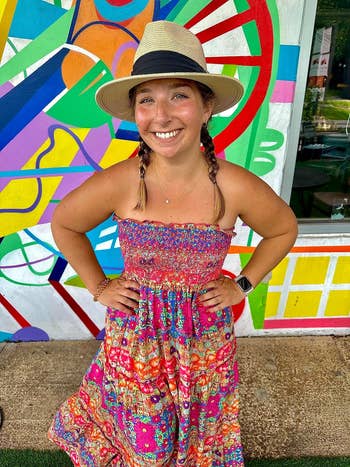 Woman in a strapless, patterned sundress and hat stands before a vibrant mural, smiling. Perfect summer outfit inspiration