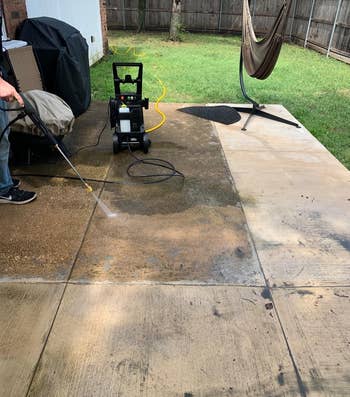 Person uses a pressure washer on a partially cleaned concrete with one section already cleaner and brighter