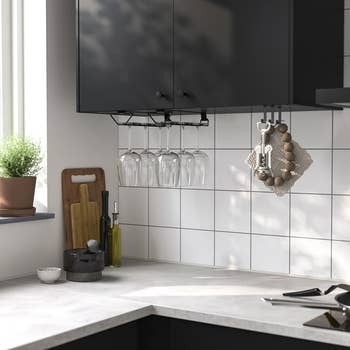 Kitchen with a hanging wine glass rack under a cabinet, showcasing organized kitchenware and countertop accessories next to a small potted plant