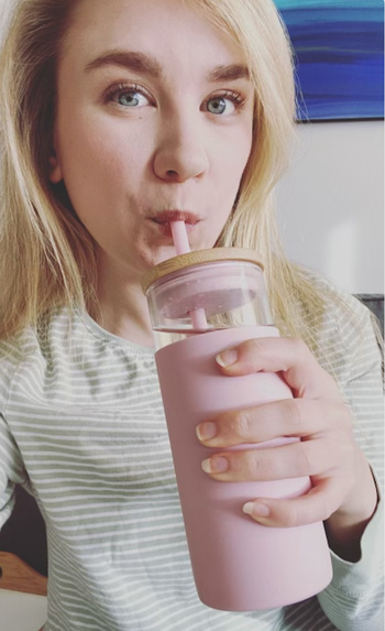 Editor holding glass tumbler with pink silicone lining and pink straw 