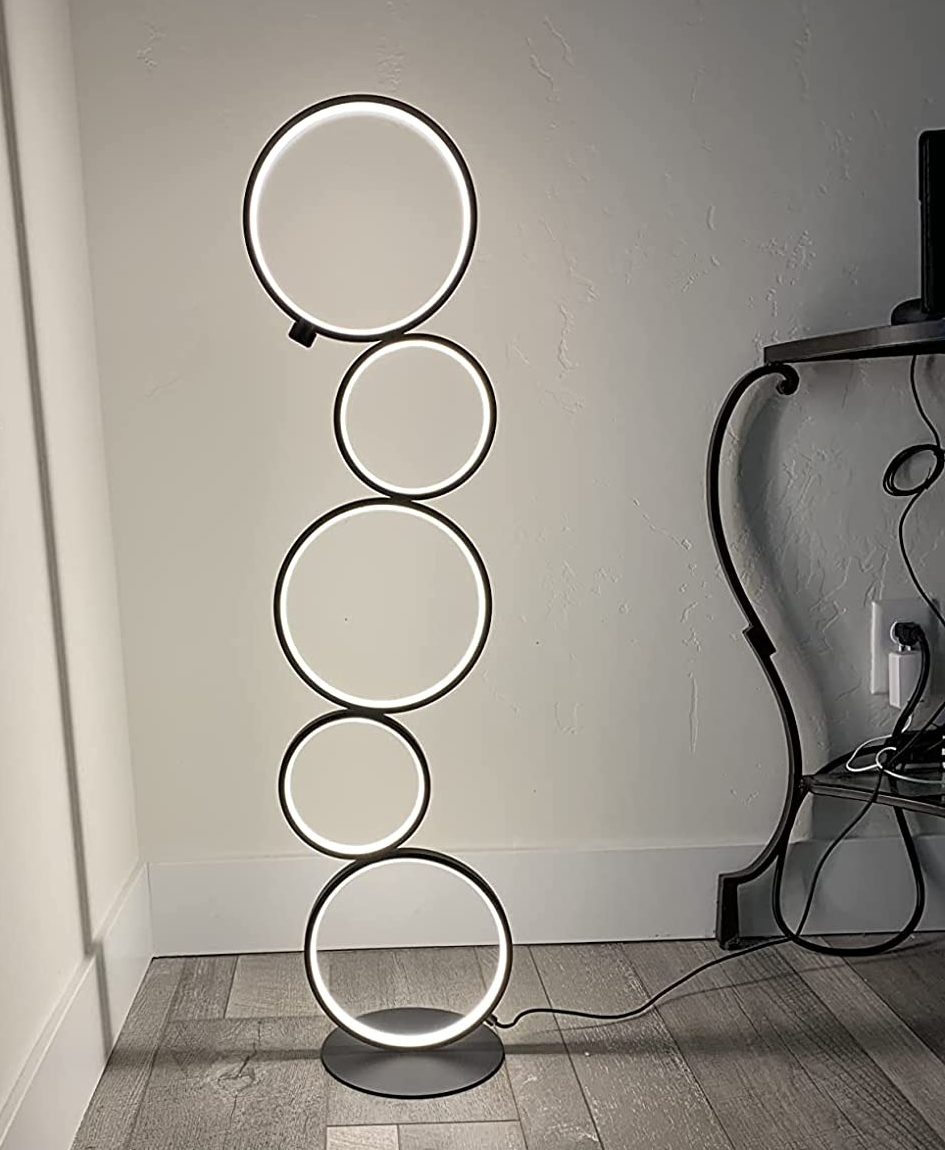 Reviewer image of stacked circular modern floor lamp plugged in and illuminating corner of white wall next to side accent table