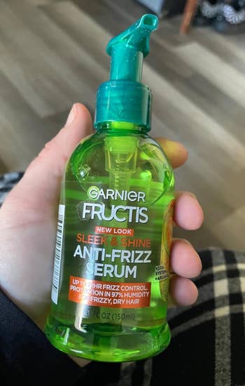 Hand holding Garnier Fructis Sleek & Shine Anti-Frizz Serum bottle, promising 97% humidity extortion and frizz power for adust hair