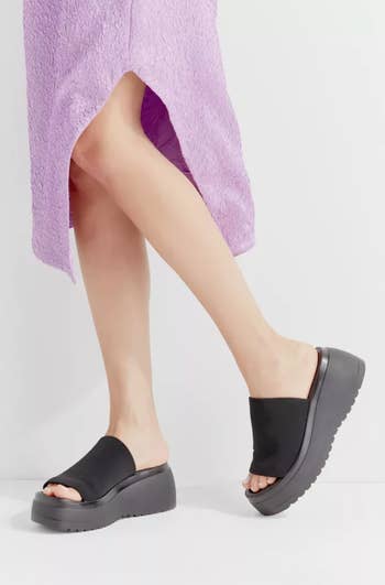 model in same chunky slide-on sandals in black with fluffy purple midi dress