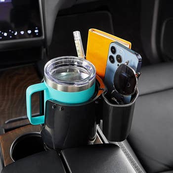 the cup holder expander with storage box in the car, holding a mug as well as sunglasses, phone, and wallet