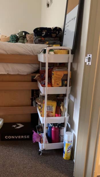 Rolling cart successful a dorm country with snacks and cleaning supplies. Items see cereal boxes, Wheat Thins, h2o bottles, and disinfecting wipes