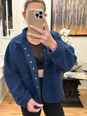 Person in a plush blue jacket and black leggings taking a mirror selfie, covering face with phone