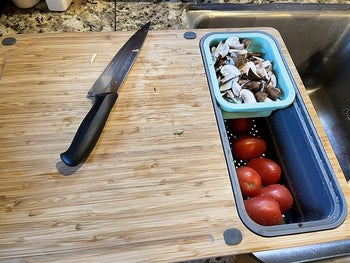 the cutting board hanging over the sink with sliced mushrooms in one container and whole tomatoes in the other