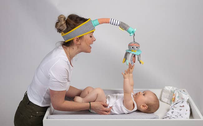 model wearing the headband while a baby on a changing table reaches for the octopus-shaped stuffed toy