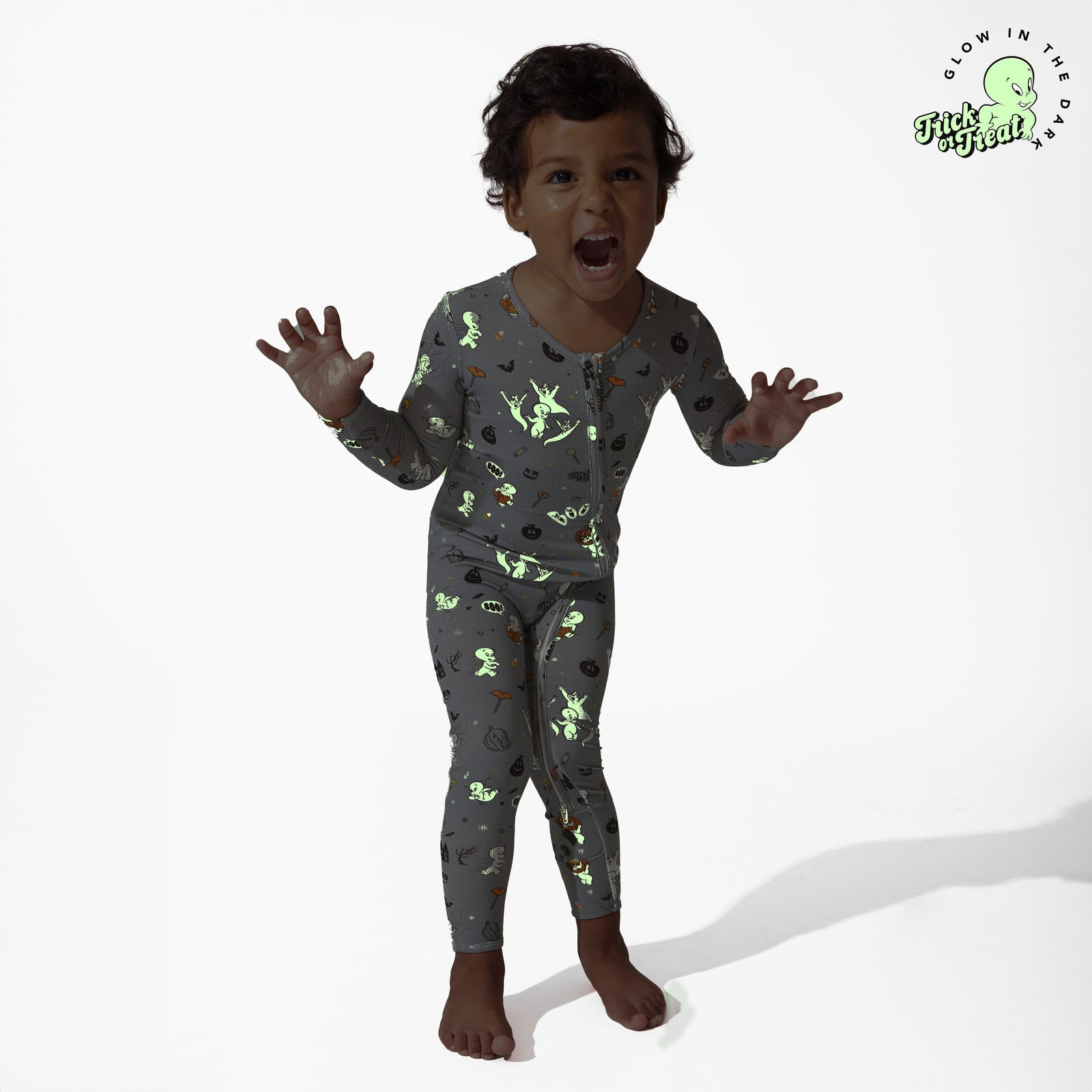 Anak yang mengenakan piyama bermotif menyala dalam gelap berpose lucu dengan tangan terangkat, menunjukkan kegembiraan. Cocok untuk belanja baju tidur anak
