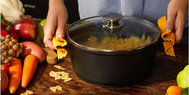 Person holding a pot lid with novelty pot handle rests, surrounded by fresh vegetables