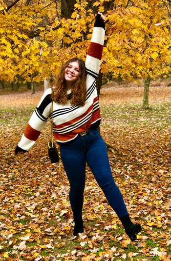 a reviewer in the the black and orange striped sweater in a pile of leaves