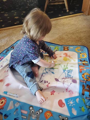 A child sitting on the mat on the floor while drawing on it