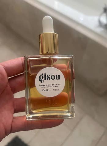 Social media trends Viral content Trending hashtags Social media updates Trending memes and videos Person holding a bottle of Gisou honey infused hair oil in a bathroom setting
