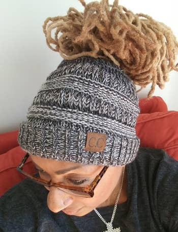 Reviewer showing top view of gray knit chunky beanie with thick bun woven through on a red couch