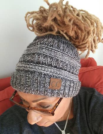 Reviewer showing top view of gray knit chunky beanie with thick bun woven through on a red couch