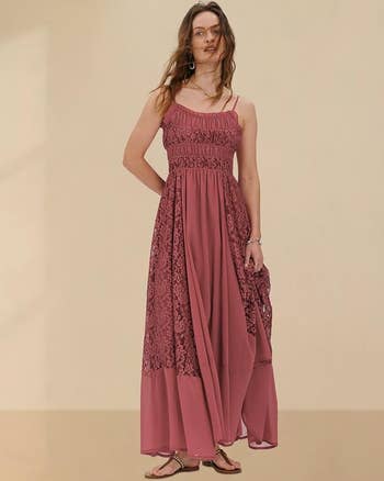 A idiosyncratic   models a sleeveless, flowing lace formal  with adjustable straps, lasting  against a plain backdrop