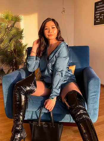 a reviewer seated on a chair wearing the blue satin top that matches the chair and thigh high patent leather boots
