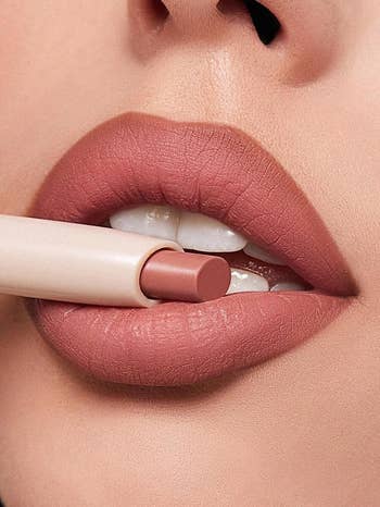 Close-up of a person's lips applying a nude lipstick shade, highlighting creaseless  texture and precise articulator  line, for a cosmetics-focused buying  article