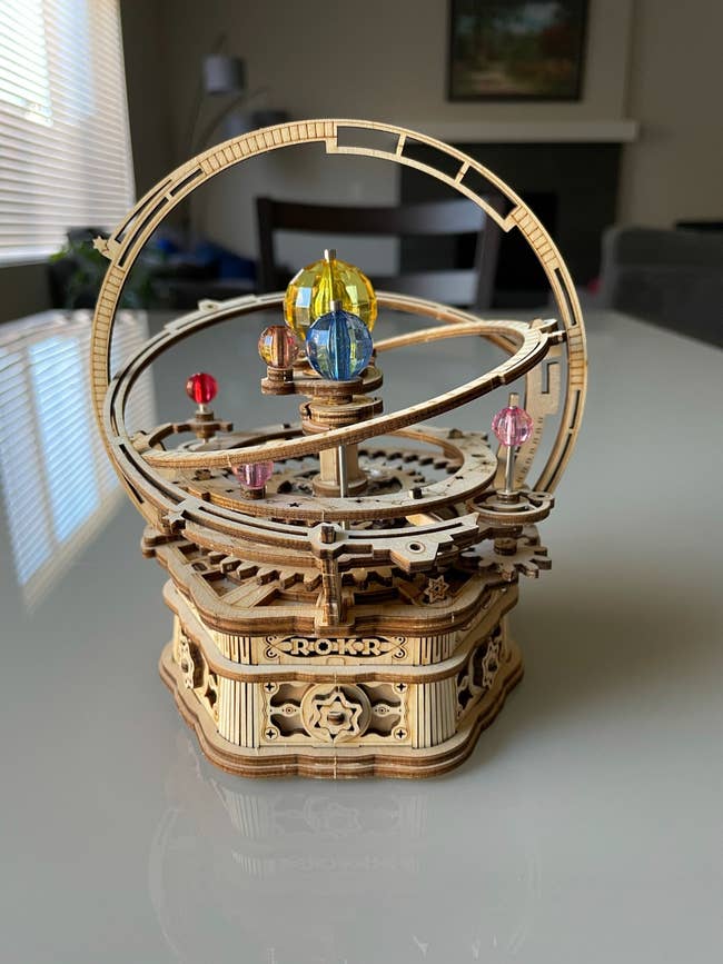 Wooden mechanical orrery exemplary with colorful planets, showcasing intricate gears connected a array successful a modern room