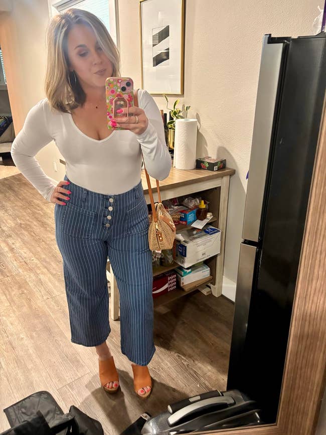 Reviewer wearing a achromatic  long-sleeve apical  and high-waisted bluish  striped pants with fastener  details, posing successful  a reflector  selfie astatine  home