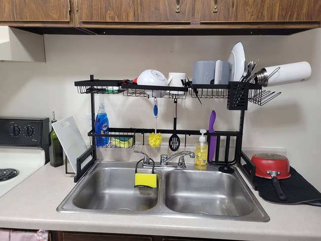 Over-sink room rack with assorted dishware, cleaning supplies, and utensils organized neatly supra a treble sink