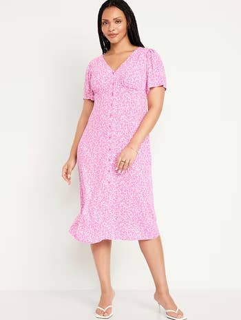Model wearing a pink floral midi dress with buttons and white sandals