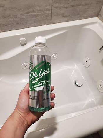 reviewer holding the bottle of Oh Yuk in front of a shiny clean tub