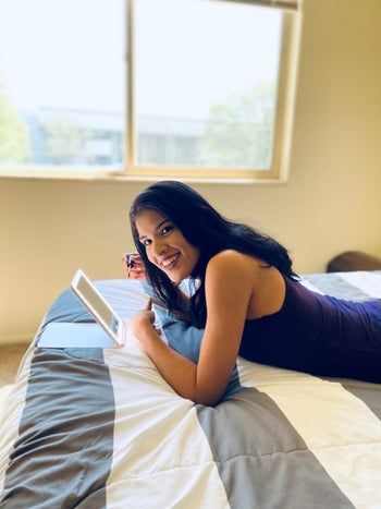 reviewer photo applying mascara using the travel mirror lying on the bed