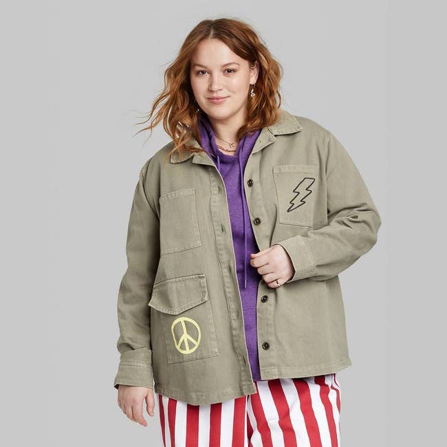 model in olive jacket with embroidered lightning bolt and yellow peace sign graphic