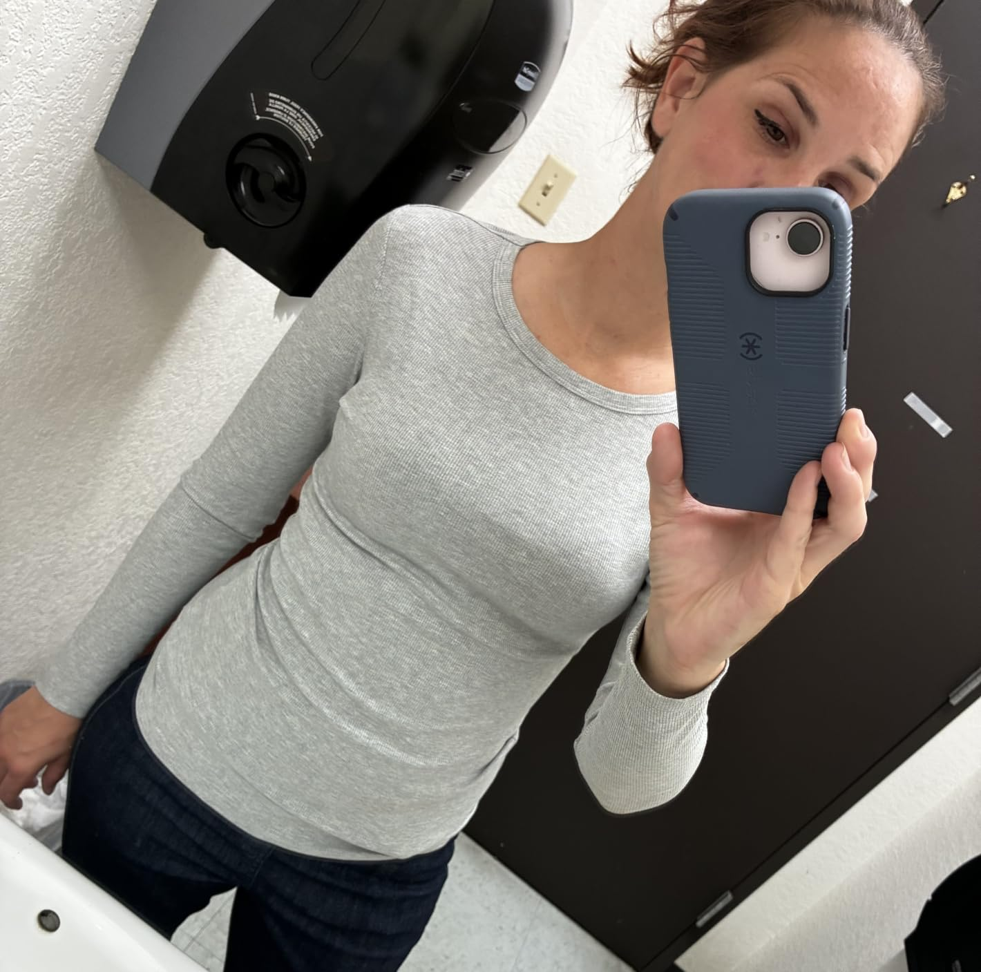 Person successful  a bath  reflector  selfie, wearing a fitted long-sleeve apical  and jeans, holding a telephone  with a disposable   camera connected  the back