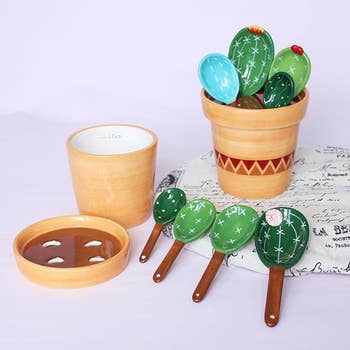 Decorative cactus-themed ceramic kitchen utensils resting in a matching pot with a spare pot and tray