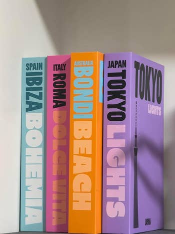 Four travel-themed books with bold titles: Spain Ibiza Bohemia, Italy Roma Dolce Vita, Australia Bondi Beach, Japan Tokyo Lights